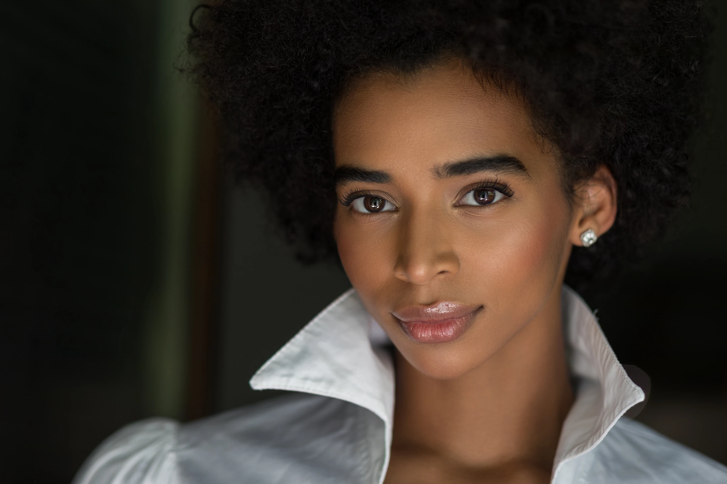Beauty portrait of a woman with natural curls in a white collar on a dark background