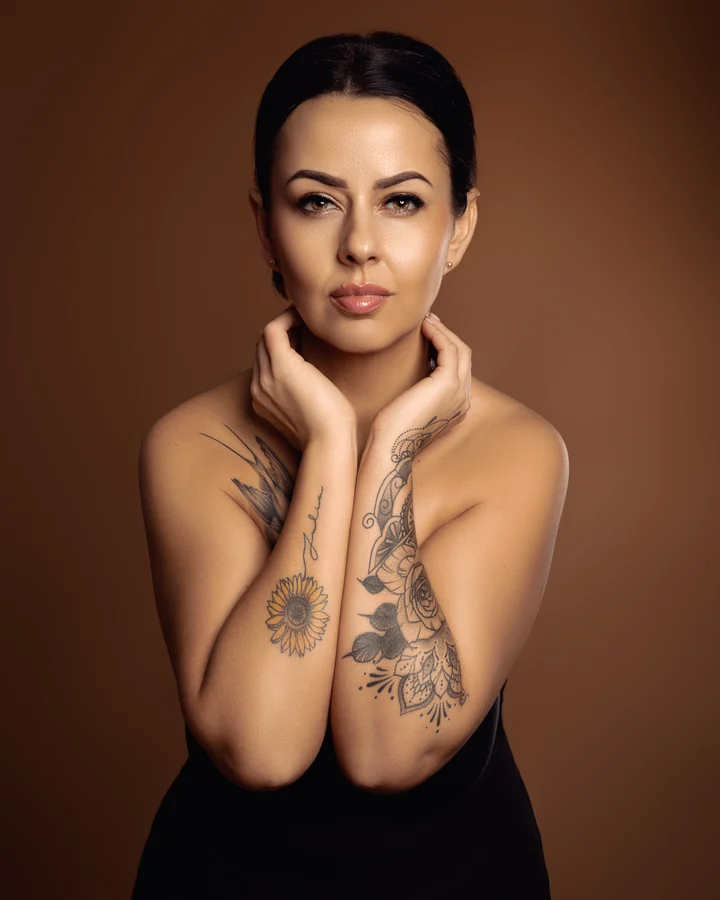 Beauty portrait of a woman with tattooed arms on a bronze background