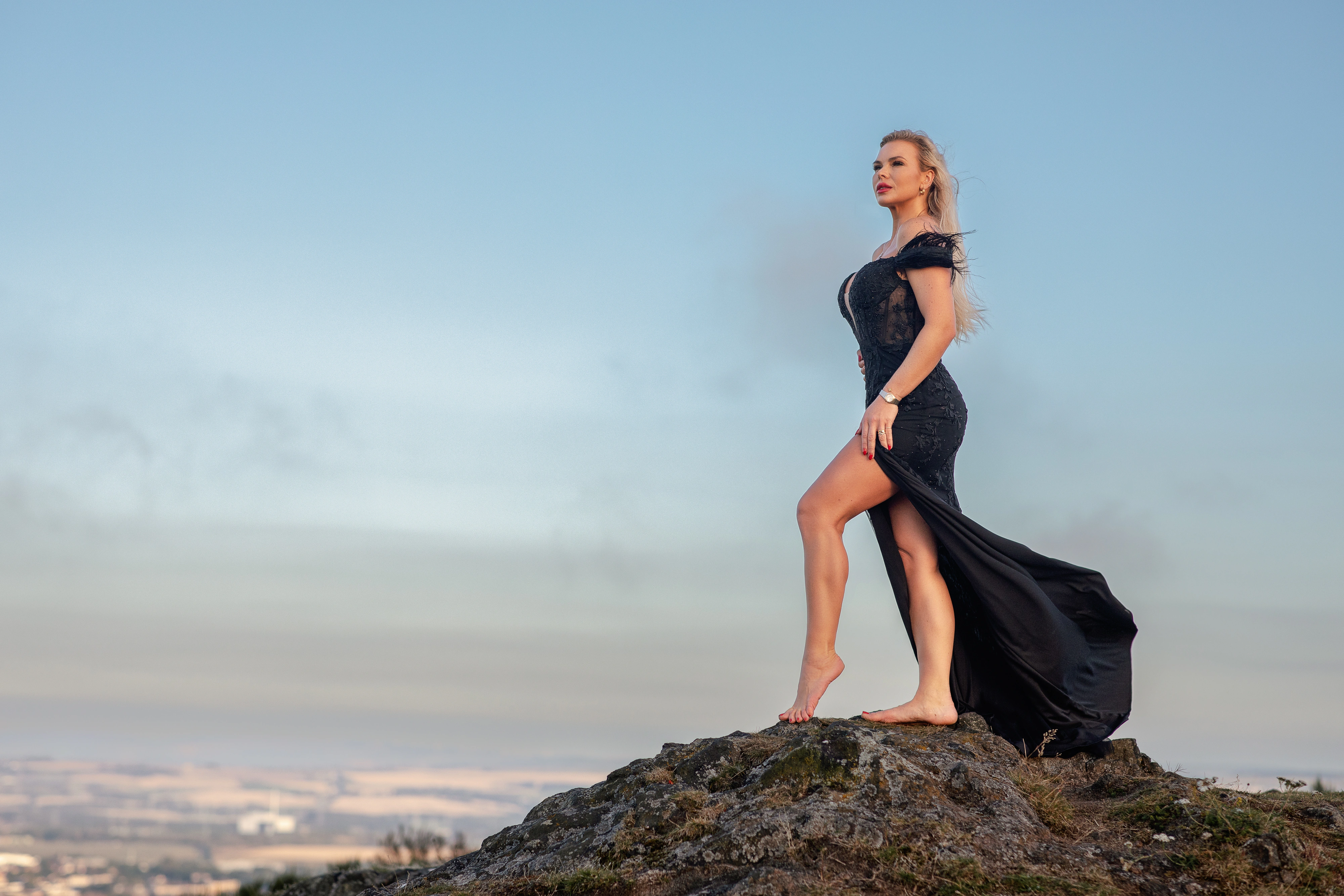 Editorial portrait of a woman in a black gown on a hilltop against a wide sky