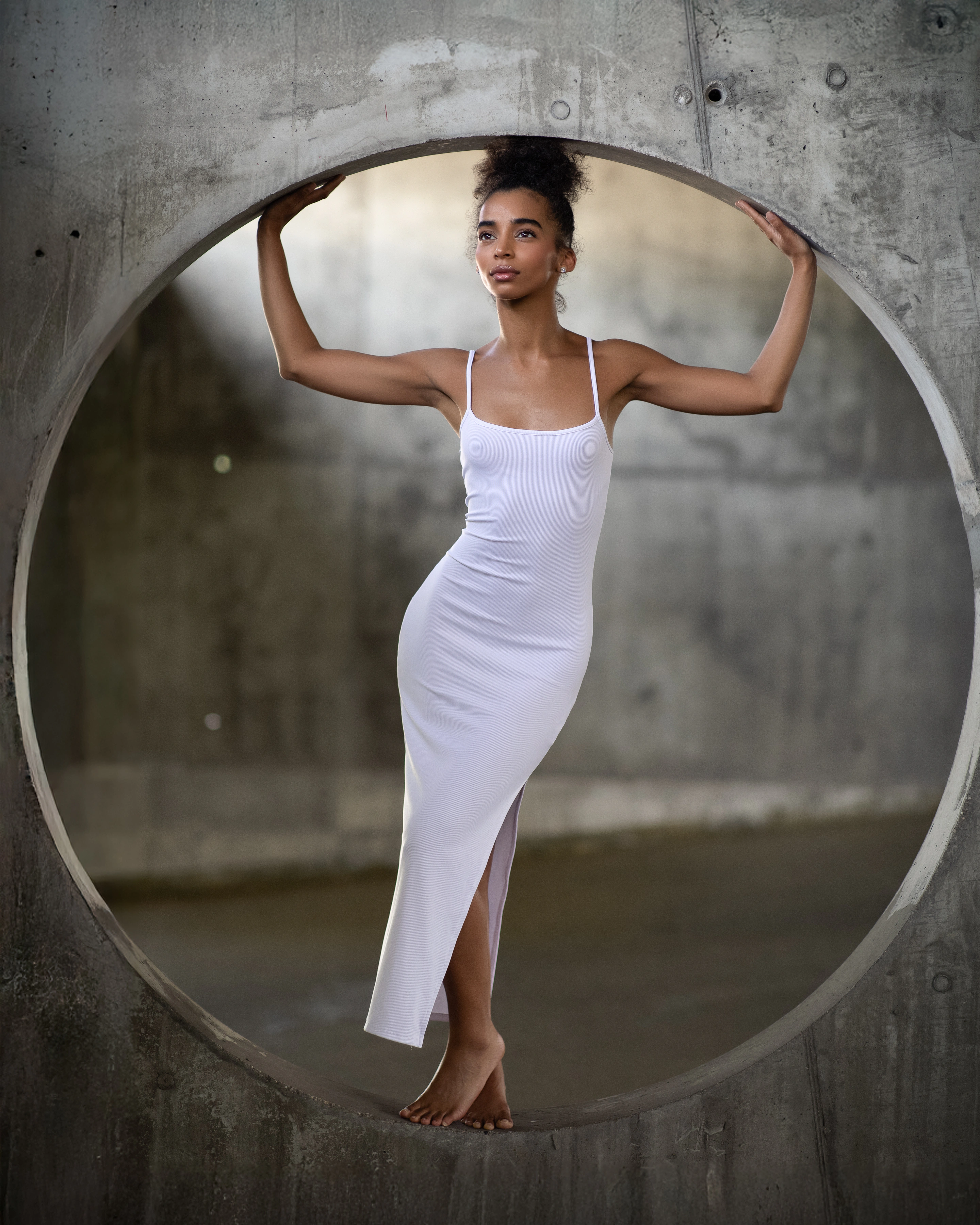 Editorial portrait of a woman in a white dress framed by a concrete circle