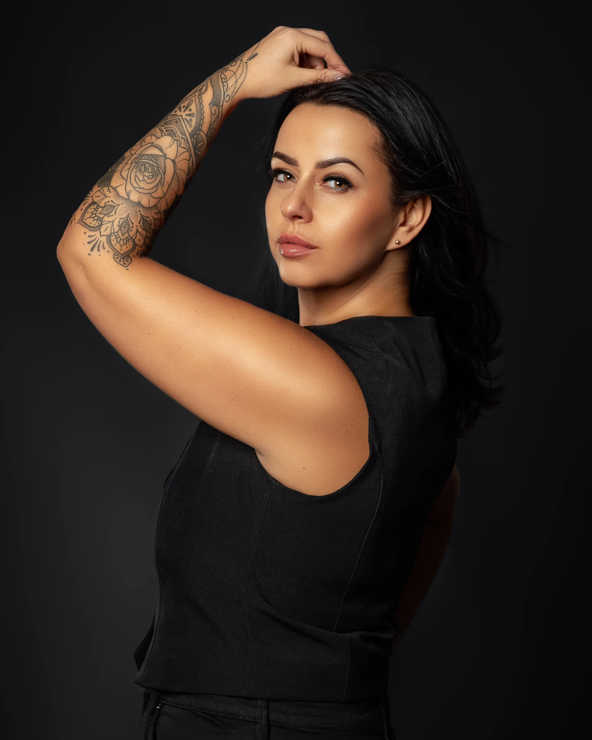 Glamour portrait of a woman with tattoos in a black top against a dark studio backdrop